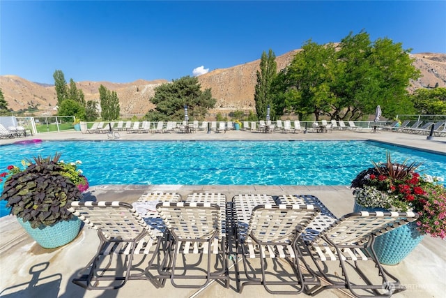 community pool with a patio area, fence, and a mountain view