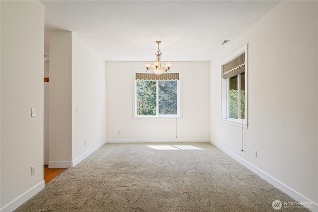 carpeted spare room featuring visible vents, baseboards, and a notable chandelier