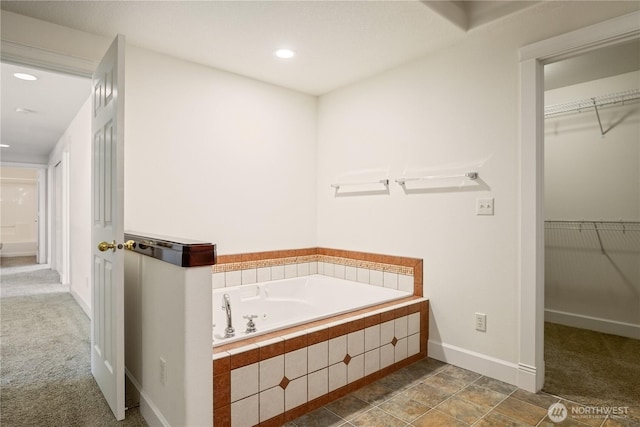 bathroom with a walk in closet, a garden tub, baseboards, and recessed lighting