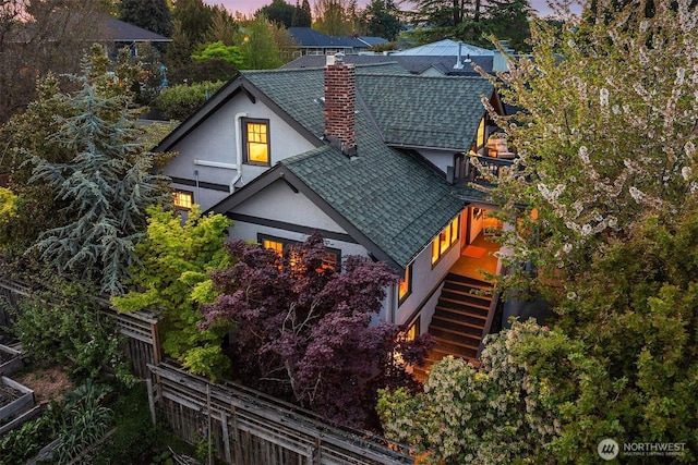 exterior space with fence, a shingled roof, stucco siding, stairway, and a chimney