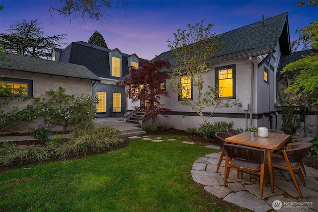 back of property with a lawn, a shingled roof, a patio area, and stucco siding