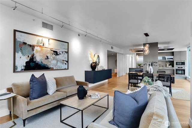 living area with track lighting, light wood-style floors, and visible vents