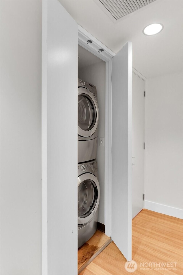 laundry room featuring visible vents, baseboards, stacked washing maching and dryer, laundry area, and wood finished floors