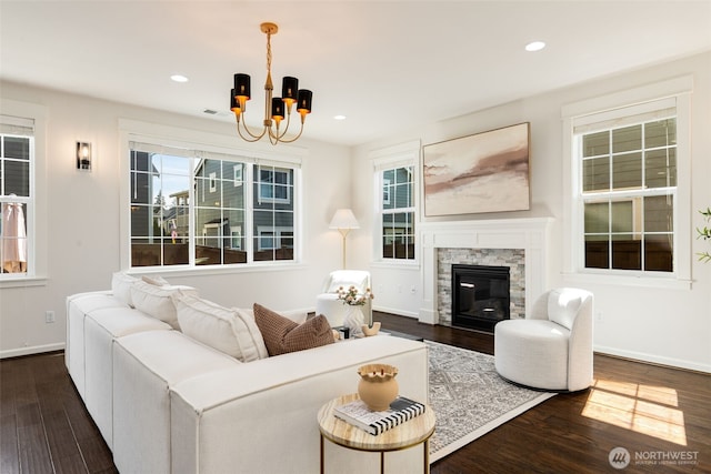 living area featuring baseboards, recessed lighting, an inviting chandelier, a stone fireplace, and dark wood-type flooring