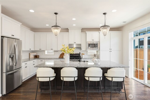 kitchen with decorative backsplash, a kitchen island with sink, appliances with stainless steel finishes, white cabinets, and under cabinet range hood
