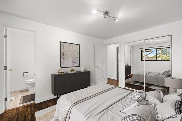 bedroom with dark wood-type flooring, a closet, ensuite bath, and baseboards