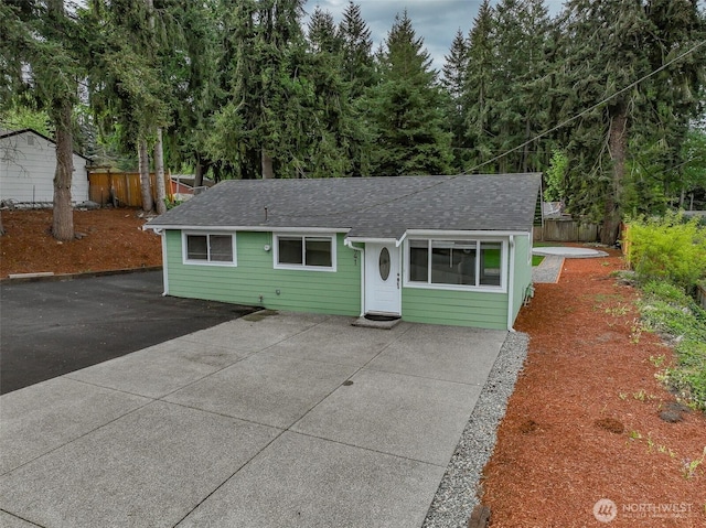 view of front of house featuring fence, a shingled roof, and a patio