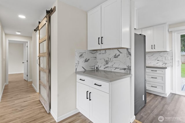 kitchen featuring light wood-type flooring, a barn door, white cabinets, decorative backsplash, and recessed lighting