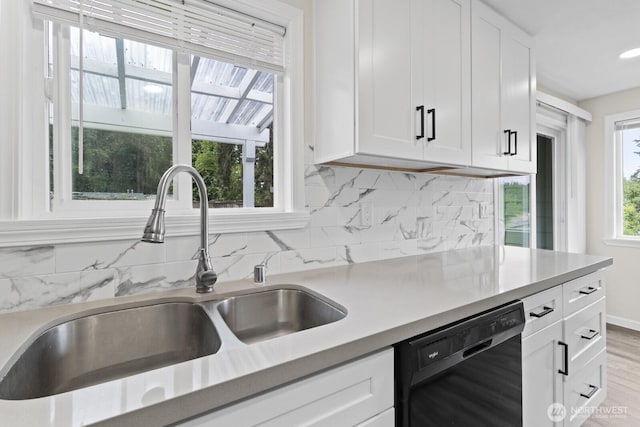 kitchen with a sink, black dishwasher, white cabinetry, backsplash, and light countertops