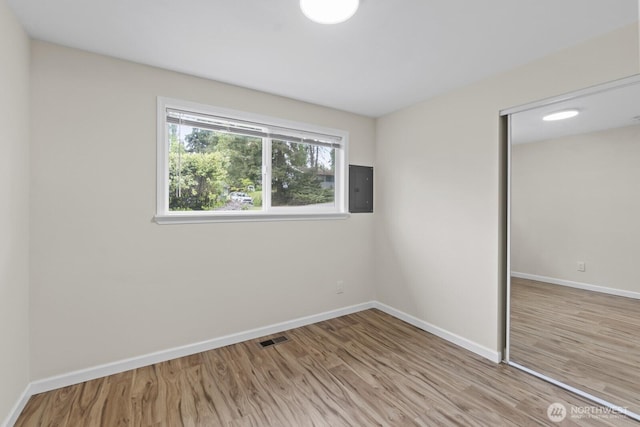 unfurnished bedroom featuring electric panel, a closet, wood finished floors, and baseboards