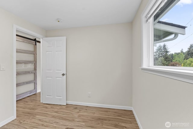 unfurnished bedroom with light wood-style floors, baseboards, and a barn door