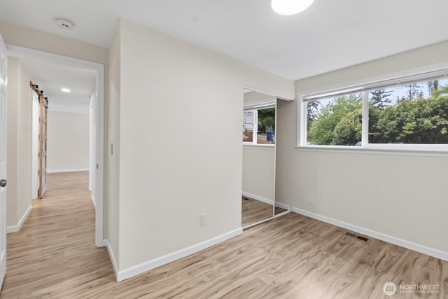 unfurnished bedroom with light wood finished floors, baseboards, a barn door, and a closet