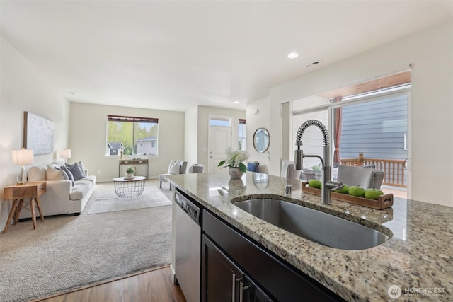 kitchen with stainless steel dishwasher, wood finished floors, a sink, open floor plan, and light stone countertops