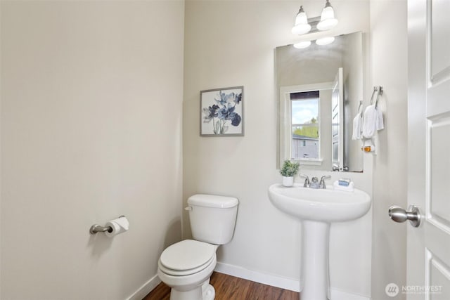 half bath with wood finished floors, toilet, baseboards, and a sink