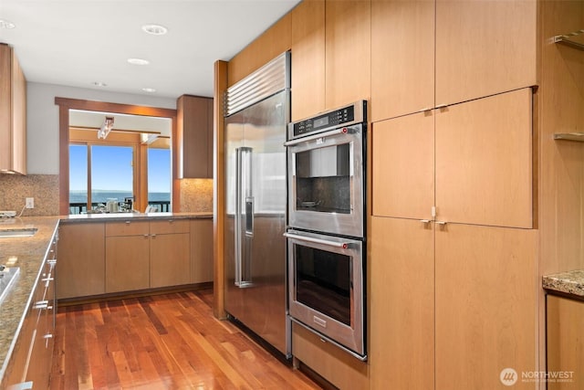 3103 Alki Ave SW, Seattle, WA 98116 - kitchen with appliances with stainless steel finishes, backsplash, wood finished floors, light stone countertops, and recessed lighting