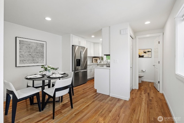 kitchen with light countertops, stainless steel fridge, light wood-style flooring, white cabinets, and recessed lighting