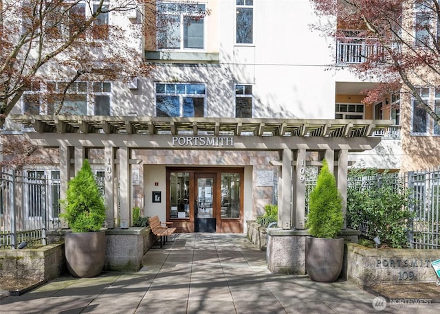 view of exterior entry featuring a pergola, stucco siding, fence, and french doors