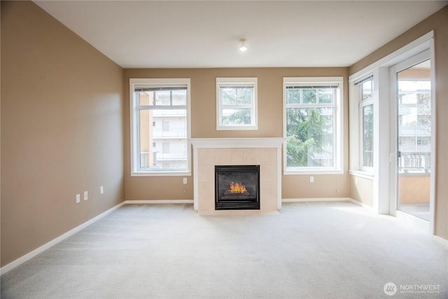 unfurnished living room with a tiled fireplace, baseboards, and carpet