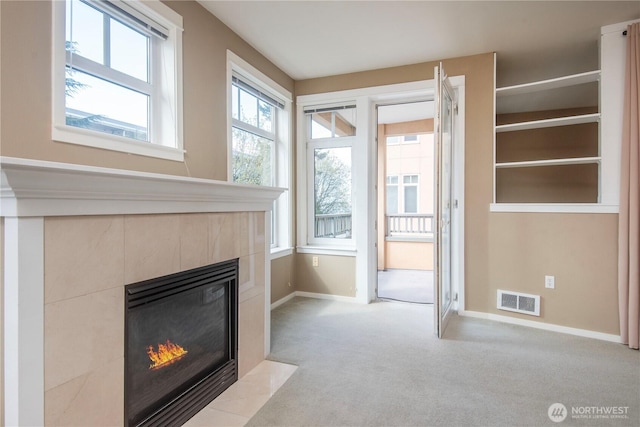 unfurnished living room featuring baseboards, a tile fireplace, visible vents, and light carpet