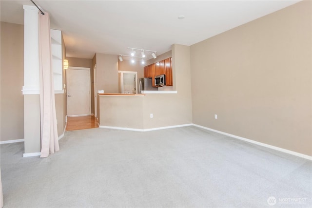 unfurnished living room featuring track lighting, baseboards, and light carpet
