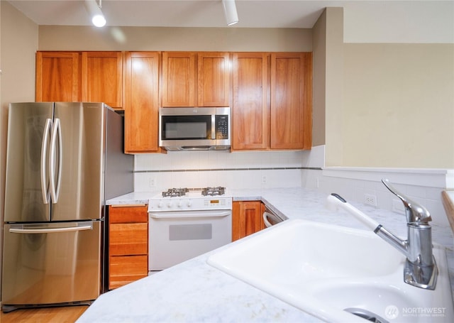 kitchen featuring light countertops, appliances with stainless steel finishes, brown cabinets, and a sink