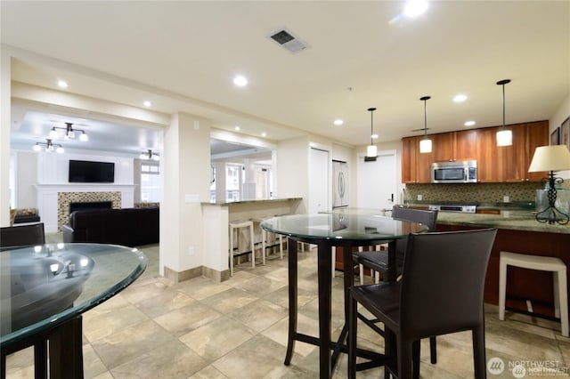 dining space featuring a tiled fireplace, visible vents, baseboards, and recessed lighting