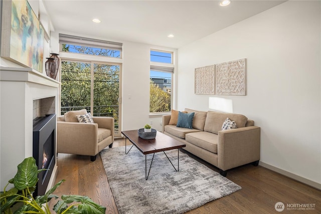 living area with recessed lighting, wood finished floors, baseboards, and a lit fireplace