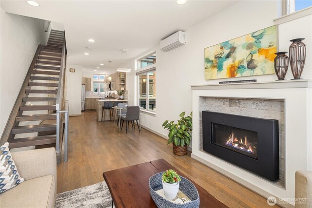 living area with recessed lighting, a wall unit AC, a fireplace, light wood-style flooring, and stairs