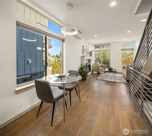dining area featuring baseboards, recessed lighting, a lit fireplace, and dark wood finished floors