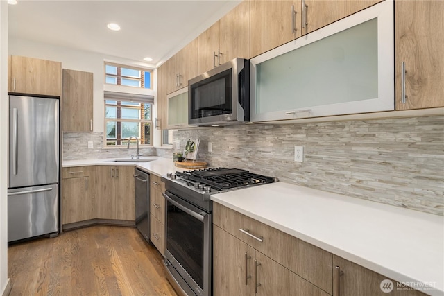 kitchen with wood finished floors, a sink, stainless steel appliances, light countertops, and backsplash