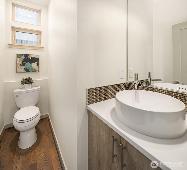 bathroom with toilet, baseboards, backsplash, wood finished floors, and vanity