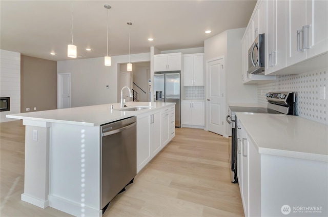 kitchen featuring tasteful backsplash, a sink, a kitchen island with sink, appliances with stainless steel finishes, and white cabinetry