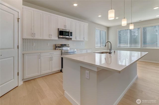 kitchen featuring light wood finished floors, stainless steel appliances, a sink, backsplash, and light countertops
