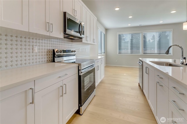 kitchen featuring light wood-style floors, tasteful backsplash, stainless steel appliances, and a sink