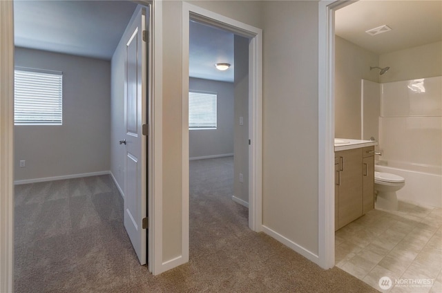 hallway with visible vents, baseboards, and light carpet