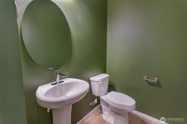 half bathroom with wood finished floors, baseboards, a sink, and toilet