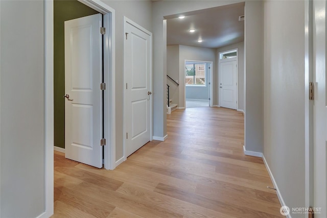 hall with baseboards, stairs, and light wood-type flooring
