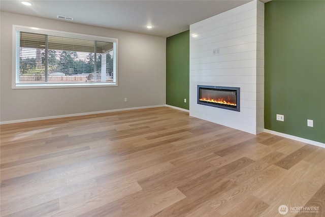 unfurnished living room with a fireplace, light wood-type flooring, visible vents, and baseboards