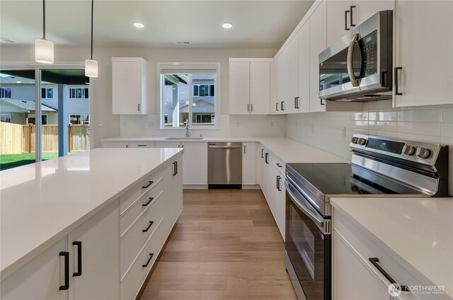 18213 35th Avenue Ct E, Tacoma, WA 98446 - kitchen featuring stainless steel appliances, light wood-type flooring, decorative backsplash, hanging light fixtures, and white cabinets