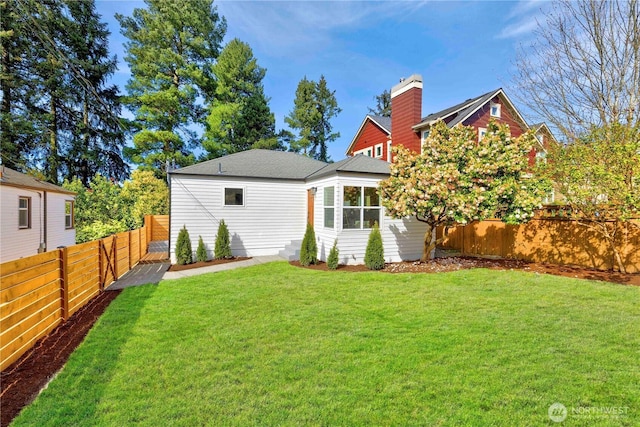 back of property with a fenced backyard, a chimney, and a yard