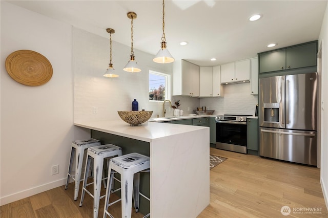 kitchen with recessed lighting, light countertops, a peninsula, light wood-style flooring, and appliances with stainless steel finishes