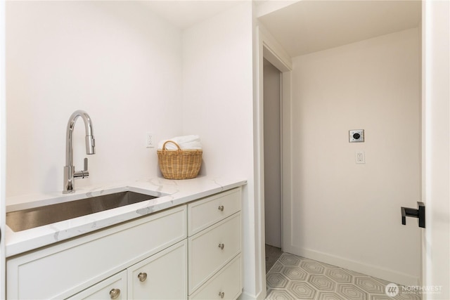 laundry room with a sink, electric dryer hookup, light floors, cabinet space, and baseboards