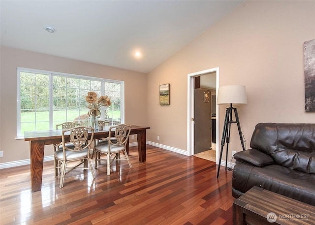 dining space featuring wood finished floors, baseboards, and high vaulted ceiling