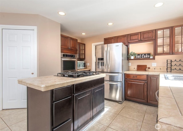 kitchen with recessed lighting, tile countertops, light tile patterned flooring, glass insert cabinets, and appliances with stainless steel finishes