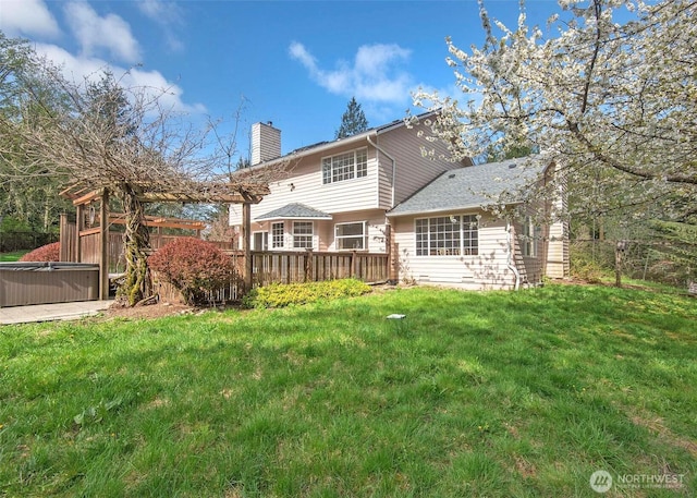 rear view of property with a wooden deck, a yard, a hot tub, and a chimney