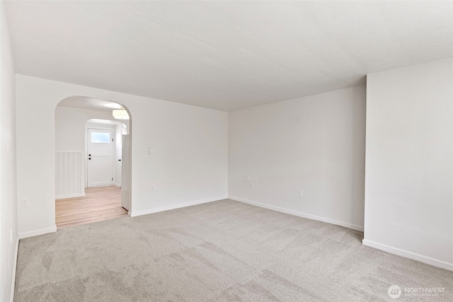 carpeted empty room featuring baseboards and arched walkways