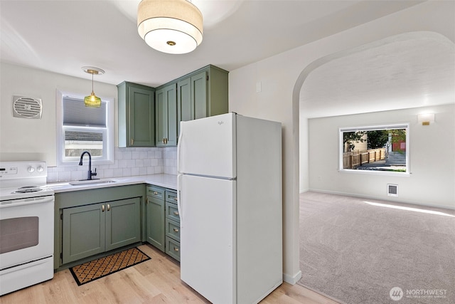 kitchen featuring arched walkways, a sink, light countertops, green cabinets, and white appliances