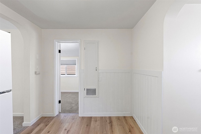 spare room with baseboards, arched walkways, wainscoting, and wood finished floors
