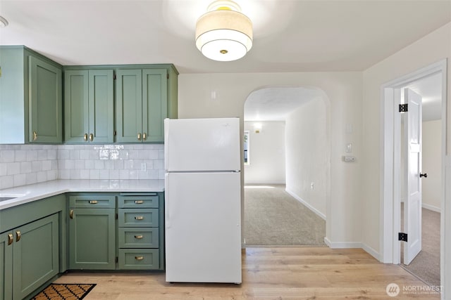kitchen with green cabinetry, light wood finished floors, light countertops, arched walkways, and freestanding refrigerator