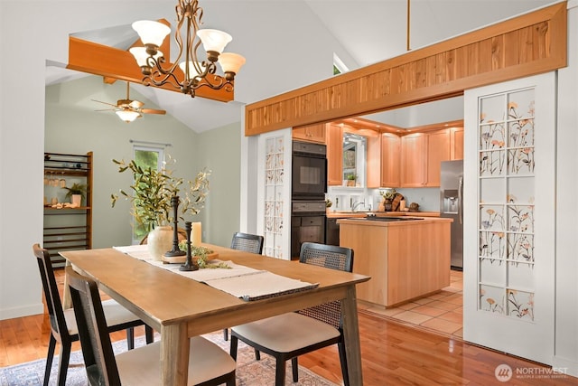 dining room featuring ceiling fan with notable chandelier, vaulted ceiling, and light wood-style flooring